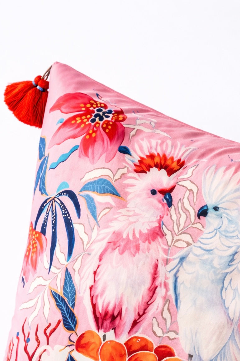 Square pink velvet cushion cover featuring illustrated cockatoos, floral motifs and red tassel corners