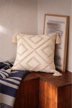 Beige square cushion with raised diamond tufted pattern and tassel corners