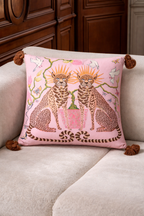 Pink velvet cushion cover with two illustrated cheetahs, sunburst halos, birds, floral branches and brown tassel corners