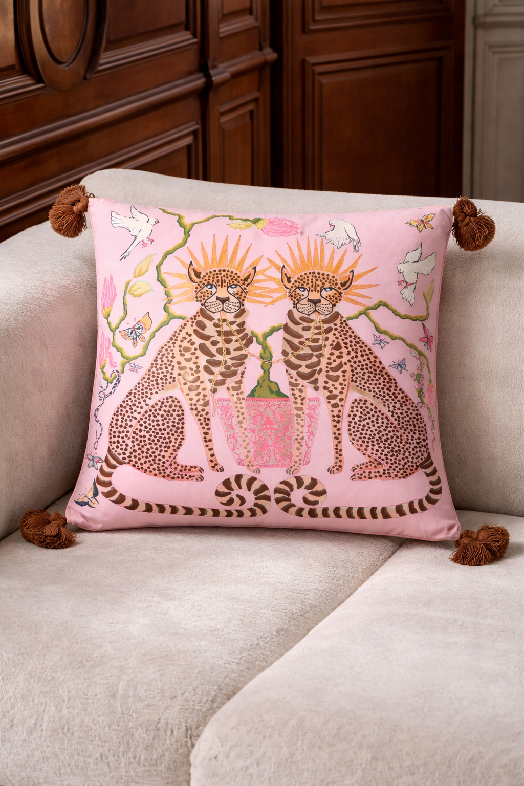 Pink velvet cushion cover with two illustrated cheetahs, sunburst halos, birds, floral branches and brown tassel corners