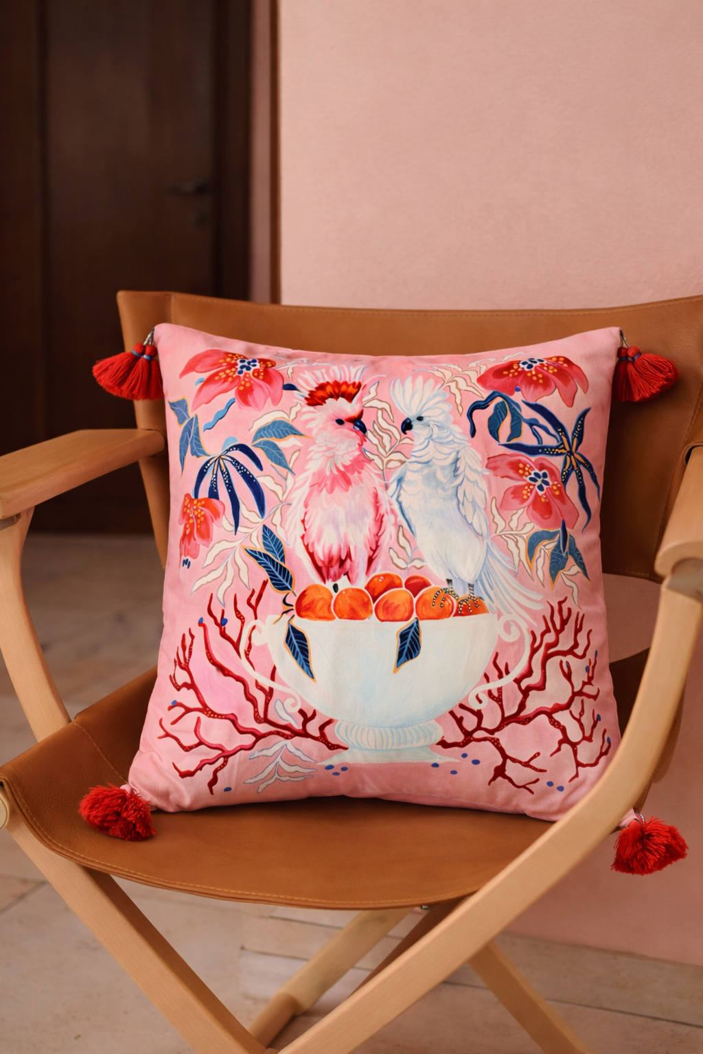 Square pink velvet cushion cover featuring illustrated cockatoos, floral motifs and red tassel corners